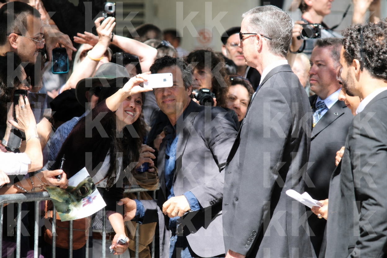 Crowd of fans with phones around a man in a grey suit at a public event