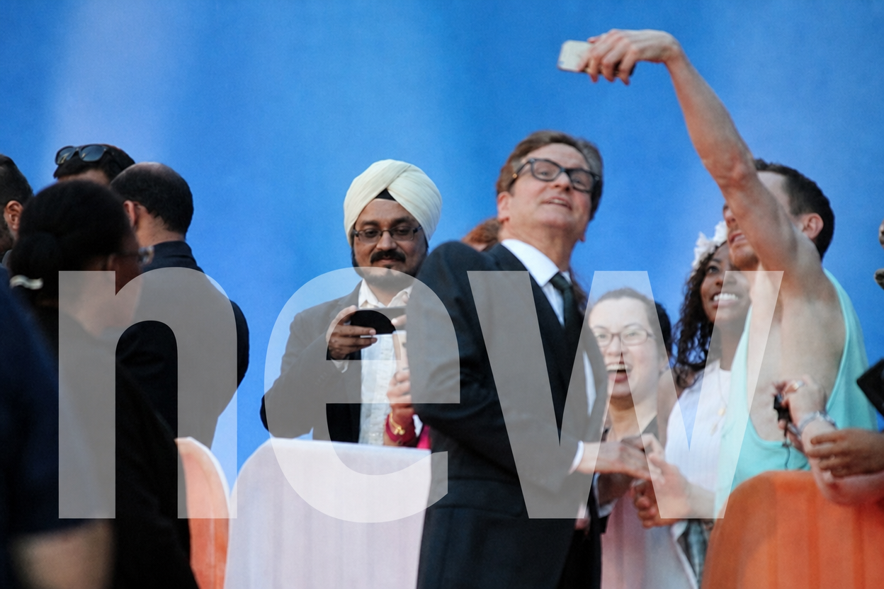 Crowd taking selfies with a man in a dark suit and glasses in front of a blue backdrop